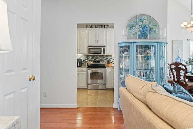kitchen with stainless steel appliances, a chandelier, light wood-type flooring, backsplash, and open floor plan