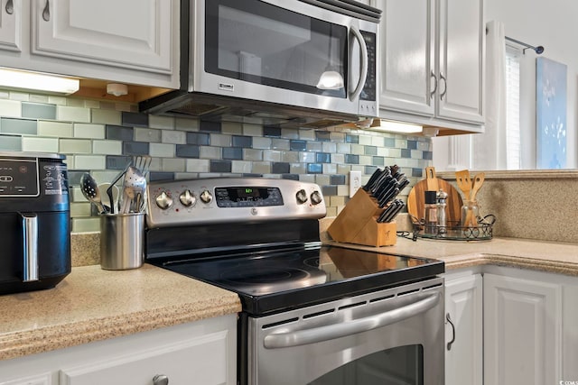 kitchen with appliances with stainless steel finishes, white cabinets, light countertops, and backsplash
