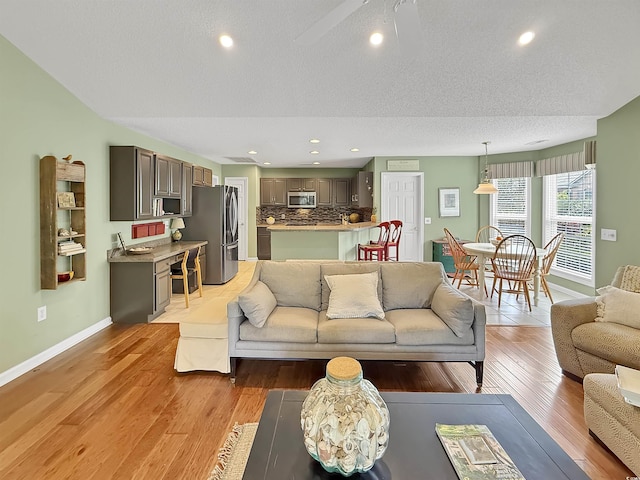 living room featuring baseboards, light wood-style floors, a textured ceiling, recessed lighting, and a ceiling fan