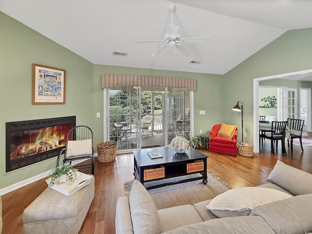 living room featuring vaulted ceiling, a glass covered fireplace, wood finished floors, a ceiling fan, and baseboards