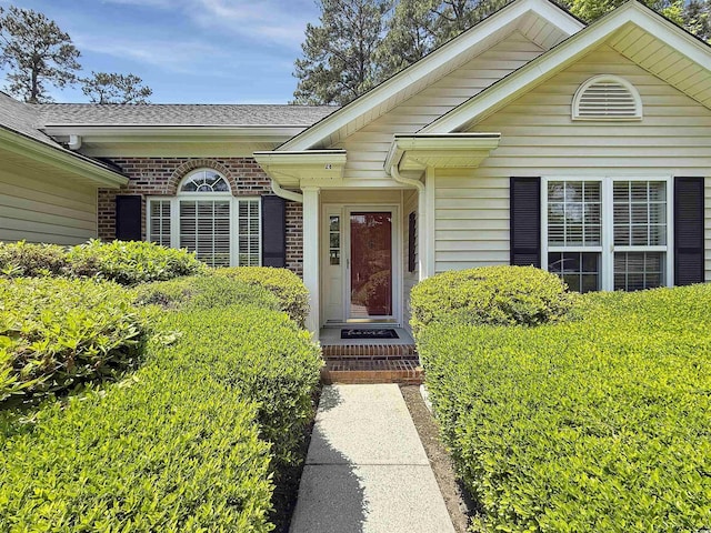 doorway to property with roof with shingles and brick siding