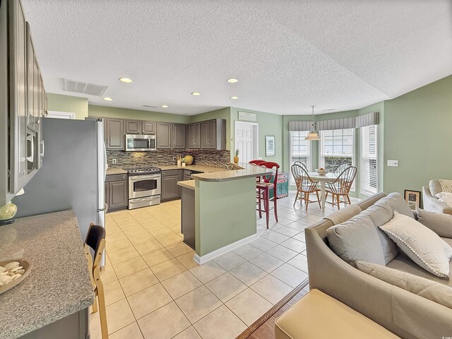 kitchen with stainless steel appliances, open floor plan, a peninsula, decorative backsplash, and a textured ceiling