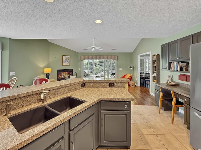 kitchen with vaulted ceiling, a sink, a textured ceiling, light tile patterned flooring, and freestanding refrigerator