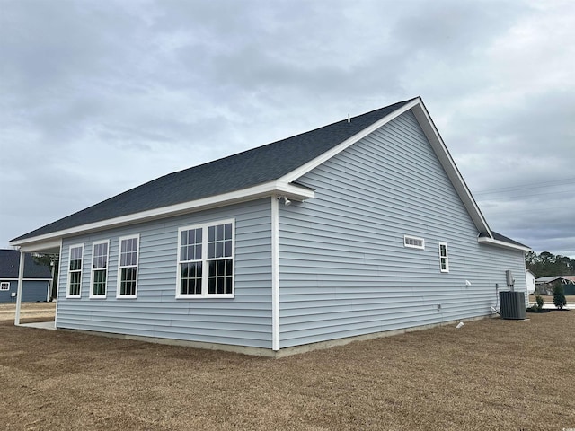 view of side of property with central AC unit and roof with shingles