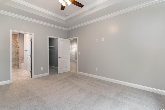 unfurnished bedroom featuring crown molding, a spacious closet, light colored carpet, a raised ceiling, and a closet