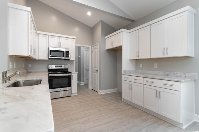 kitchen featuring stainless steel appliances, a sink, light stone counters, light wood-style floors, and high vaulted ceiling