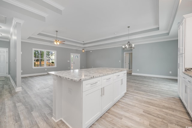 kitchen featuring a tray ceiling, open floor plan, a kitchen island, light wood-type flooring, and ornamental molding