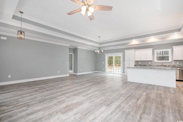 unfurnished living room featuring a raised ceiling, light wood-style floors, a chandelier, and crown molding