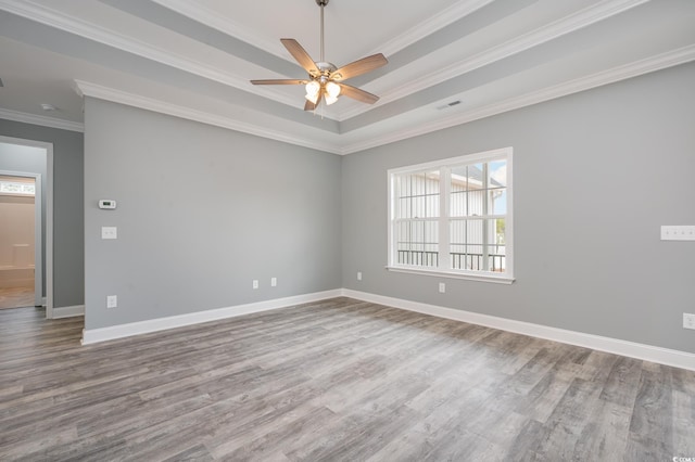 spare room with plenty of natural light, wood finished floors, ornamental molding, a raised ceiling, and ceiling fan
