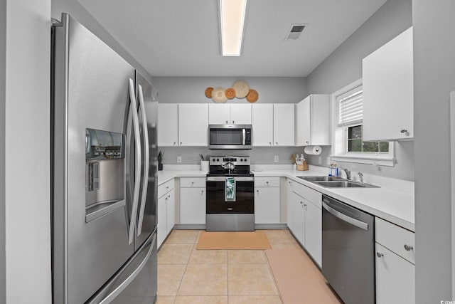 kitchen with appliances with stainless steel finishes, a sink, light countertops, white cabinetry, and light tile patterned floors