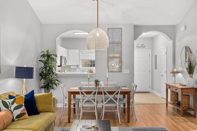dining room featuring arched walkways, light wood-style flooring, and baseboards
