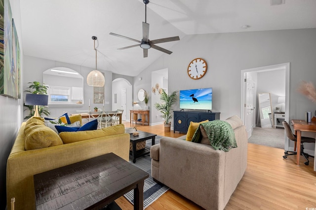 living room featuring arched walkways, a ceiling fan, light wood-type flooring, and vaulted ceiling
