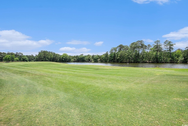 view of grassy yard featuring view of golf course, a water view, and view of wooded area
