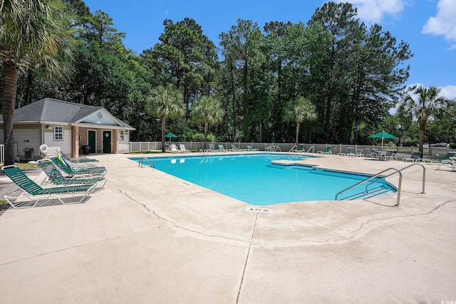 community pool with fence, a patio area, and view of wooded area