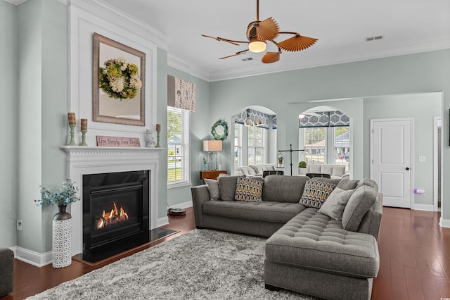 living room featuring ornamental molding, a glass covered fireplace, plenty of natural light, dark wood-style flooring, and baseboards
