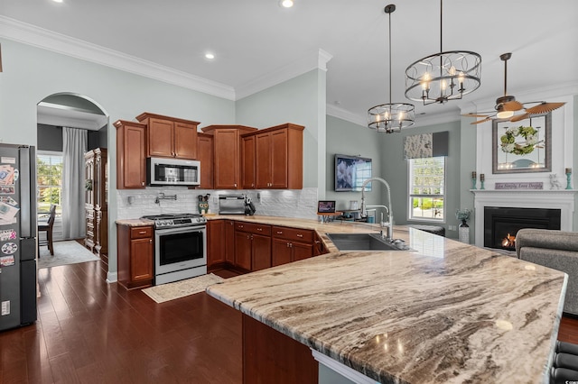 kitchen with appliances with stainless steel finishes, a sink, a peninsula, crown molding, and a warm lit fireplace