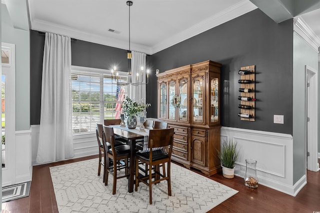dining space with wood finished floors, a chandelier, crown molding, wainscoting, and a decorative wall