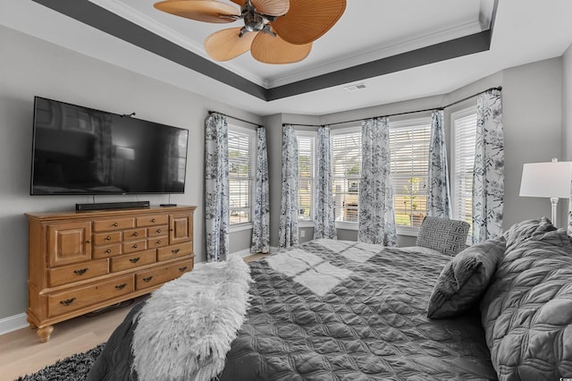 bedroom with crown molding, wood finished floors, baseboards, a tray ceiling, and ceiling fan