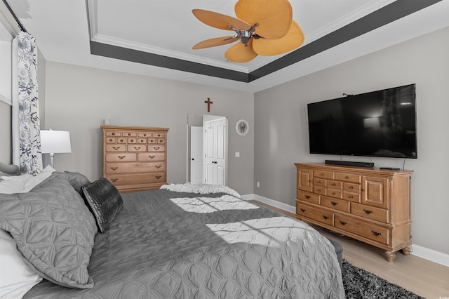 bedroom featuring wood finished floors, baseboards, crown molding, a tray ceiling, and ceiling fan