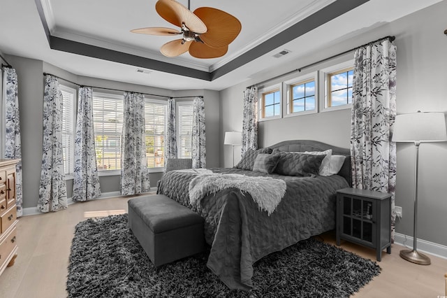 bedroom with a tray ceiling, wood finished floors, ornamental molding, baseboards, and a ceiling fan