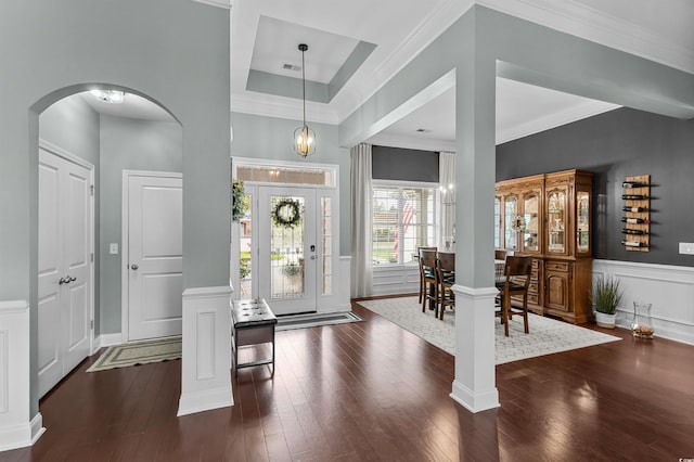 foyer entrance with arched walkways, hardwood / wood-style floors, crown molding, a wainscoted wall, and a decorative wall