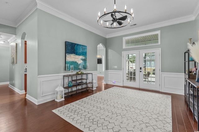 foyer with arched walkways, ornamental molding, a chandelier, wood finished floors, and a wainscoted wall