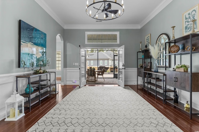 entryway featuring a chandelier, arched walkways, ornamental molding, wood finished floors, and a wainscoted wall