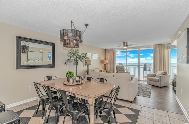 dining space with a textured ceiling, light tile patterned floors, a ceiling fan, expansive windows, and a water view