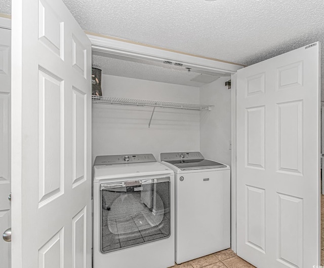 clothes washing area with a textured ceiling, independent washer and dryer, and light tile patterned floors