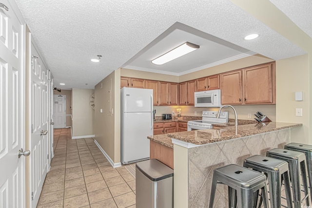 kitchen featuring white appliances, a sink, light tile patterned floors, a kitchen breakfast bar, and a peninsula