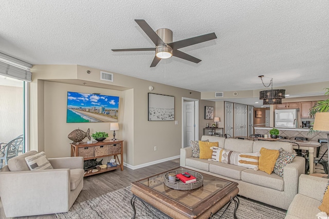 living room with a textured ceiling, a ceiling fan, light wood-style flooring, baseboards, and a chandelier