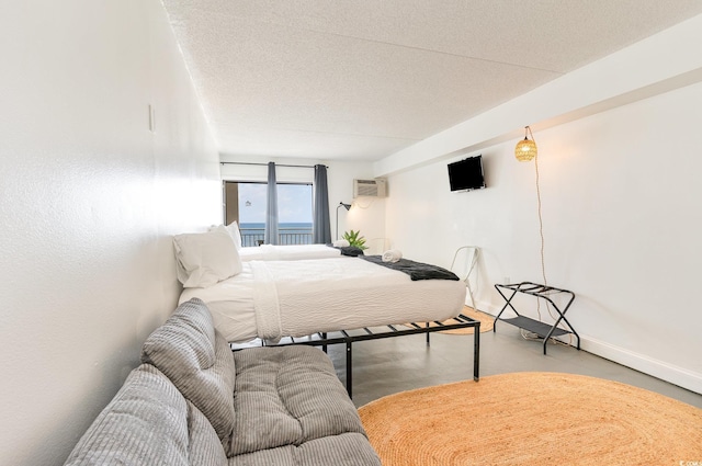 bedroom featuring finished concrete flooring, an AC wall unit, baseboards, and a textured ceiling