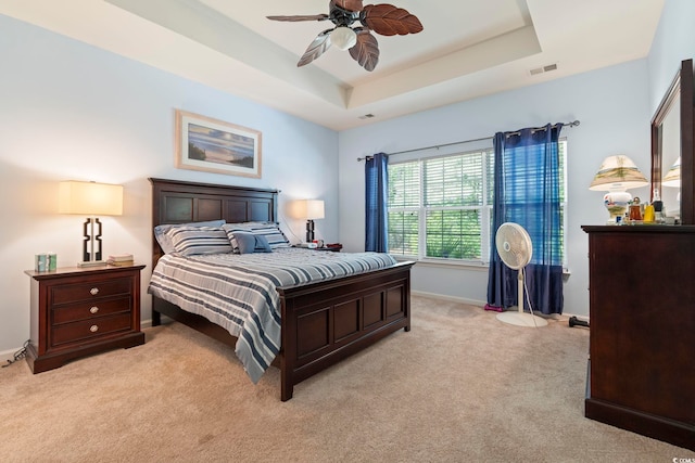 bedroom with light carpet, baseboards, a tray ceiling, and a ceiling fan