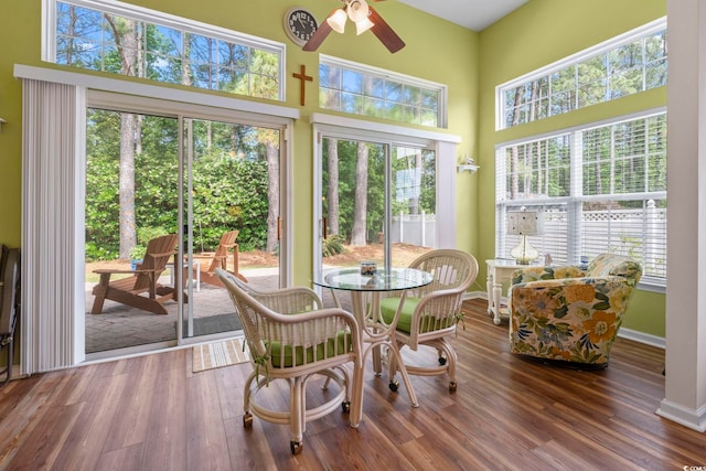 sunroom / solarium featuring a high ceiling, wood finished floors, and baseboards