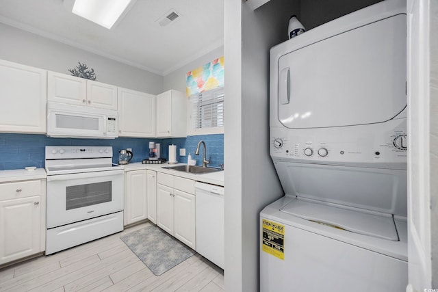 kitchen with white appliances, stacked washing machine and dryer, a sink, white cabinets, and crown molding