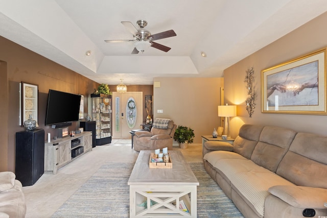 carpeted living room with a raised ceiling and ceiling fan