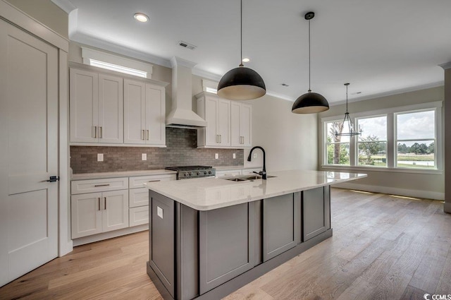 kitchen featuring a sink, decorative backsplash, wall chimney exhaust hood, crown molding, and white cabinets