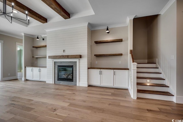 unfurnished living room featuring ornamental molding, light wood-style flooring, beam ceiling, stairs, and baseboards