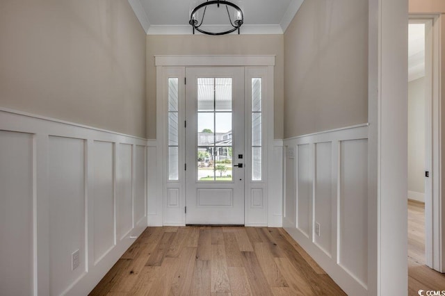 doorway with a decorative wall, a wainscoted wall, light wood-type flooring, crown molding, and a chandelier