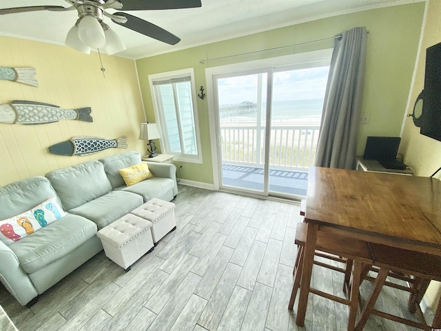 living room featuring crown molding, light wood finished floors, a ceiling fan, a water view, and baseboards