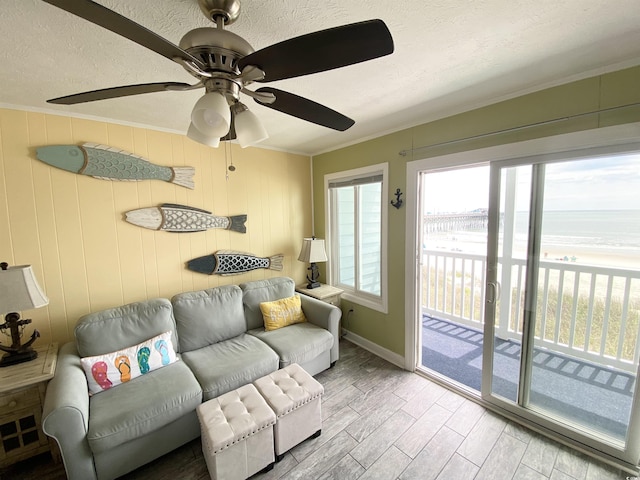 living area with ornamental molding, view of water and beach, wood finished floors, baseboards, and ceiling fan