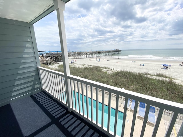 balcony with view of water and beach and view of pool