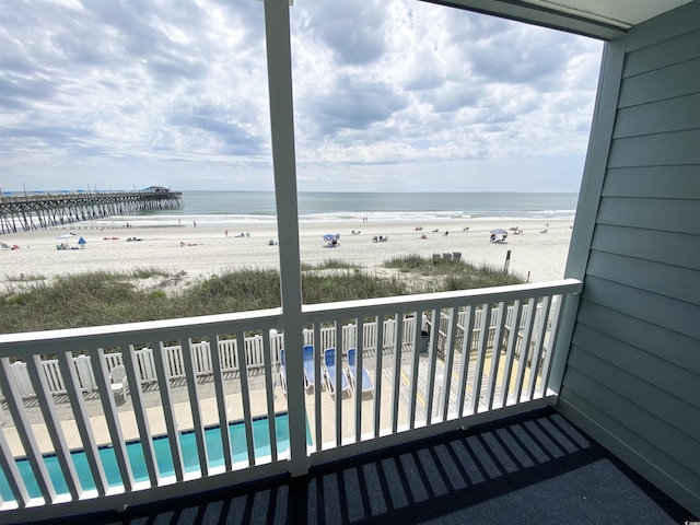 balcony with view of water and beach and view of pool area