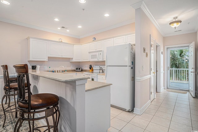 kitchen with white appliances, a peninsula, a breakfast bar area, white cabinetry, and light tile patterned floors