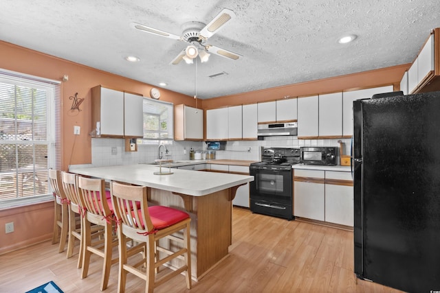 719 Juniper Dr, Myrtle Beach, SC 29575 - kitchen with black appliances, under cabinet range hood, a peninsula, decorative backsplash, and a textured ceiling