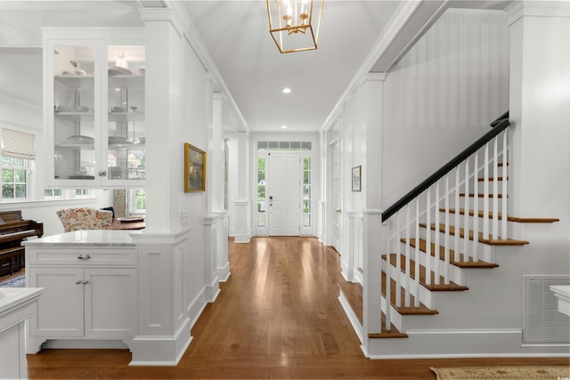 entryway featuring healthy amount of natural light, wood finished floors, ornamental molding, stairway, and a chandelier