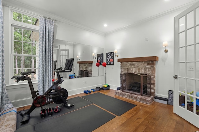 workout room featuring a fireplace, wood finished floors, crown molding, and baseboards