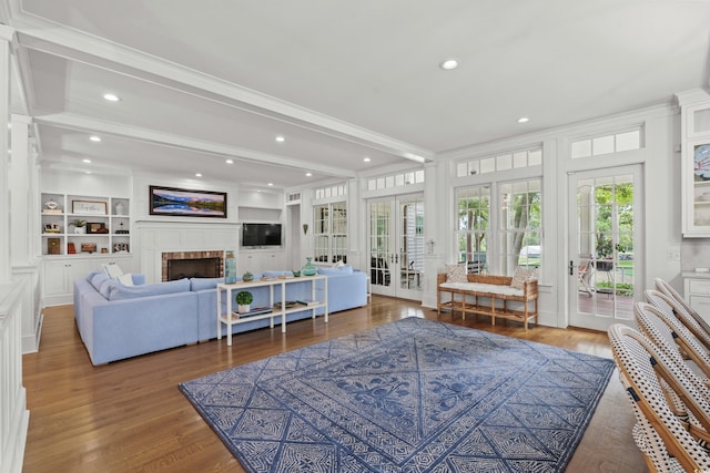 living area featuring french doors, plenty of natural light, a fireplace, wood finished floors, and beam ceiling
