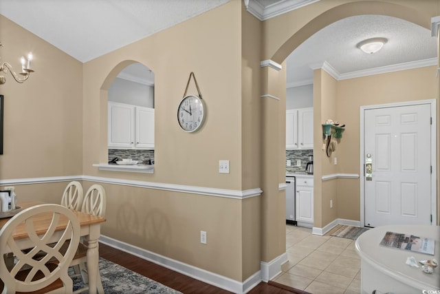 foyer entrance featuring arched walkways, crown molding, a textured ceiling, light wood finished floors, and baseboards