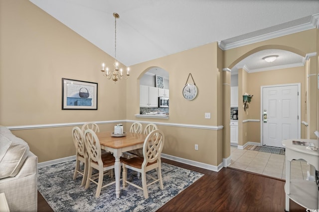 dining room featuring arched walkways, a chandelier, crown molding, light wood finished floors, and baseboards
